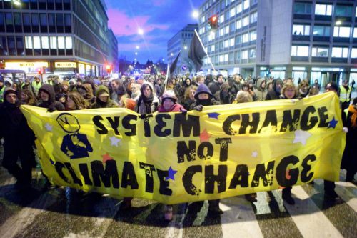 Image of protesters at a climate change rally holding a banner that states System Change not Climate Change